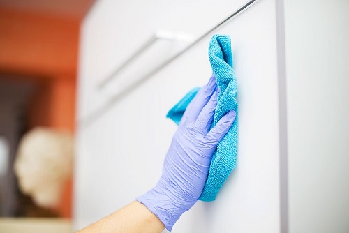  Person’s hand with a glove on wiping down a surface with a cloth to disinfect the surface